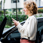 A woman stands near the open door of her vehicle while using her mobile phone. 